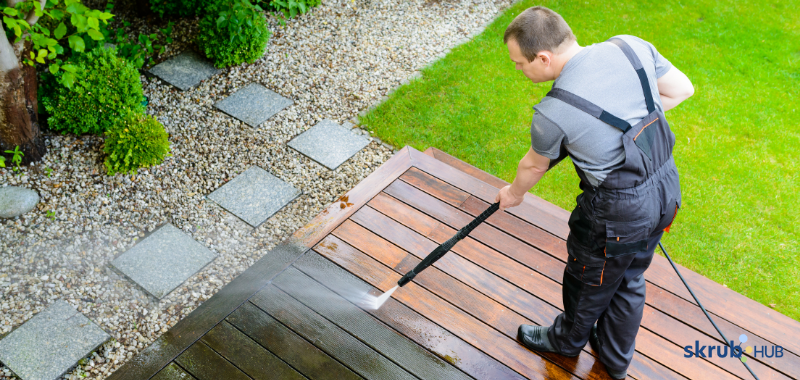 Professional cleaner using pressure washer to clean a wooden patio